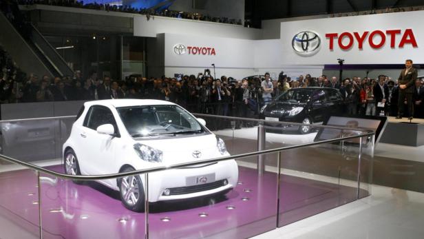 Ein weißer Toyota iQ auf einer Automesse vor Publikum.