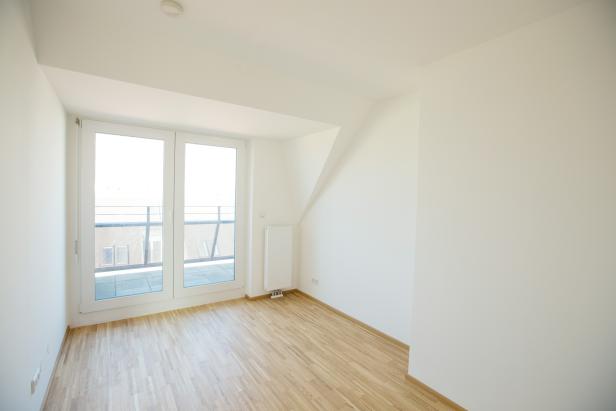 Ein leerer, heller Raum mit Holzboden und Zugang zu einem Balkon.