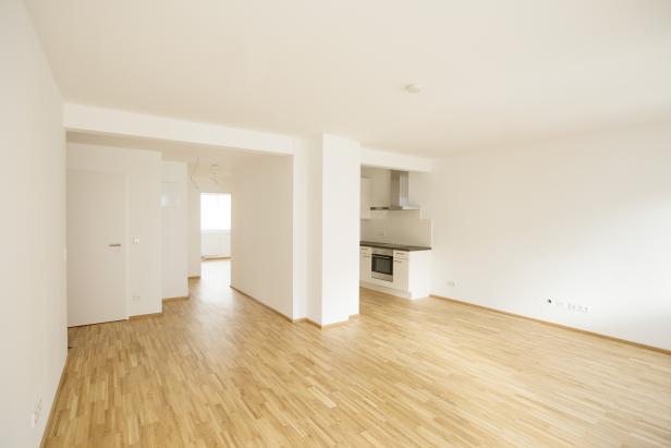 Ein leerer, heller Raum mit Holzboden und einer kleinen Küchenzeile.