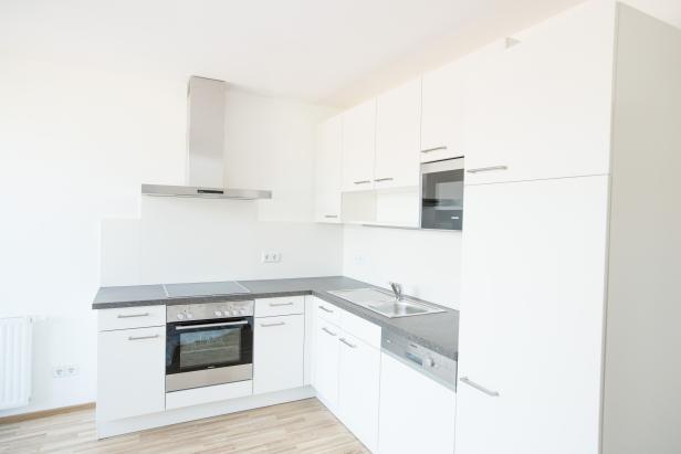 Eine moderne, helle Küche mit weißen Schränken und grauer Arbeitsplatte.