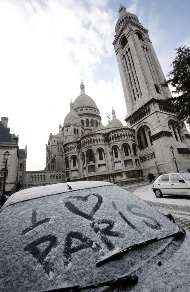 Auf der schneebedeckten Windschutzscheibe eines Autos steht „I ❤️ Paris“ vor Sacré-Cœur.
