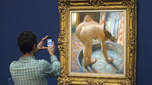 Ein Mann fotografiert ein Gemälde von Edgar Degas mit dem Titel „Das Bad“ in einem Museum.