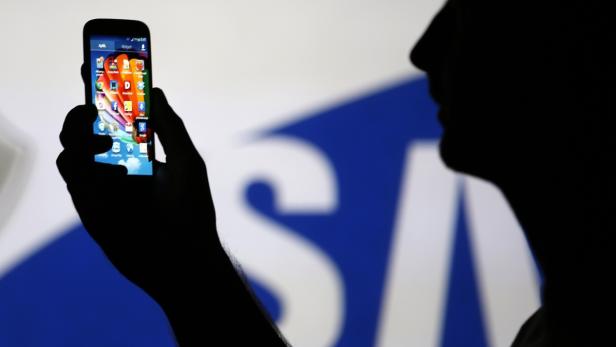 File photo illustration of a man is silhouetted ag Die Silhouette einer Person, die ein Smartphone vor einem Samsung-Logo hält.