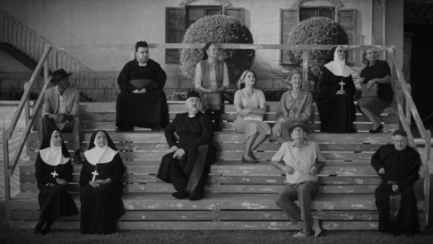 Eine Gruppe von Menschen, darunter Nonnen und Priester, sitzt auf einer Treppe in Schwarzweiß.