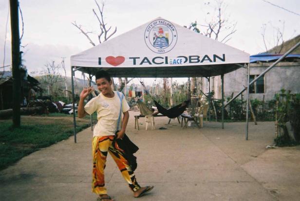 Ein lächelnder Mann posiert vor einem Zelt mit der Aufschrift „I ❤️ Tacloban“.