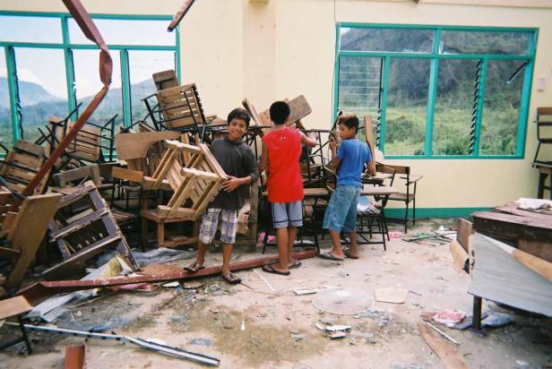 Drei Jungen räumen in einem Klassenzimmer nach einem Unwetter auf.