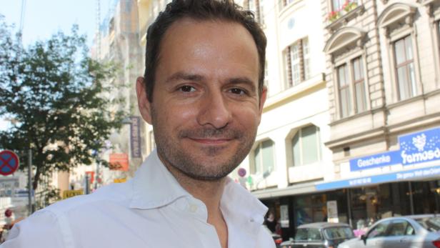 Ein Mann in einem weißen Hemd steht vor einem Gebäude in der Stadt.