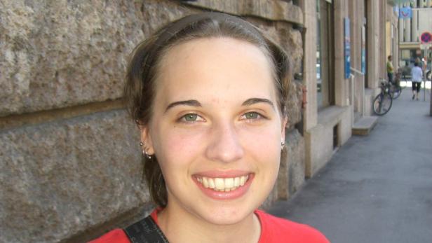 Eine lächelnde junge Frau steht vor einem Gebäude in einer Stadt.