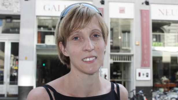 Eine Frau mit Sonnenbrille auf dem Kopf steht vor einem Gebäude.