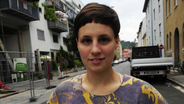 Eine junge Frau mit kurzen, dunklen Haaren steht auf einer Straße.