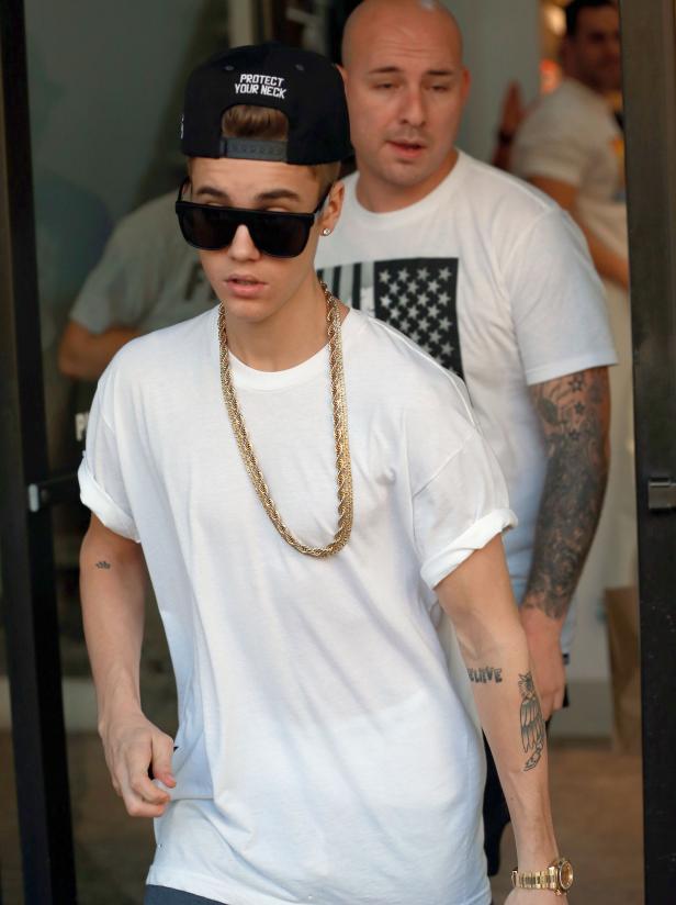 Justin Bieber mit Sonnenbrille und Goldkette, begleitet von einem Bodyguard.