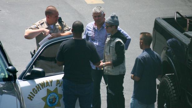Ein Polizist der California Highway Patrol spricht mit Justin Bieber und anderen Personen neben einem Streifenwagen.