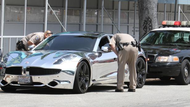 Zwei Polizisten inspizieren einen verspiegelten Fisker Karma neben einem Streifenwagen.