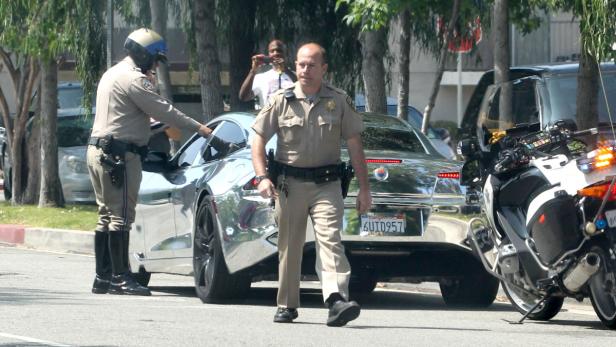 Zwei Polizisten stehen neben einem silbernen Auto und einem Motorrad.