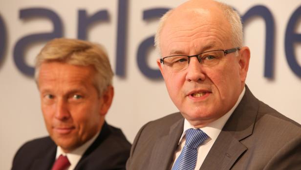 Zwei Männer in Anzügen vor einem Firmenlogo.