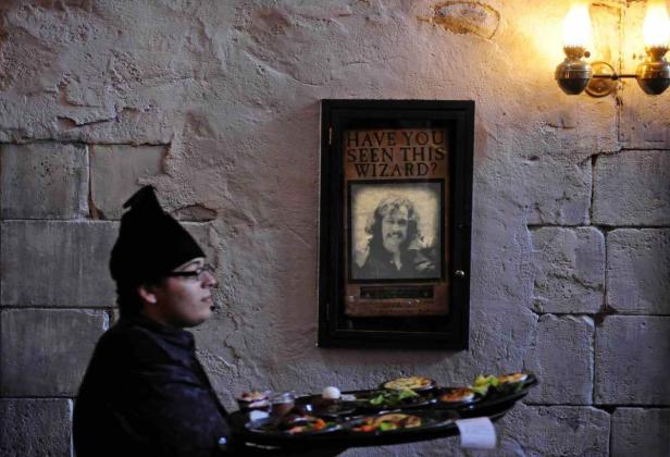 Ein Kellner mit Speisen steht vor einem „Have You Seen This Wizard?“-Poster.