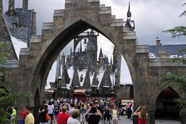 Blick durch einen steinernen Torbogen auf die Menschenmenge in Hogsmeade, einem Themenbereich von Harry Potter.