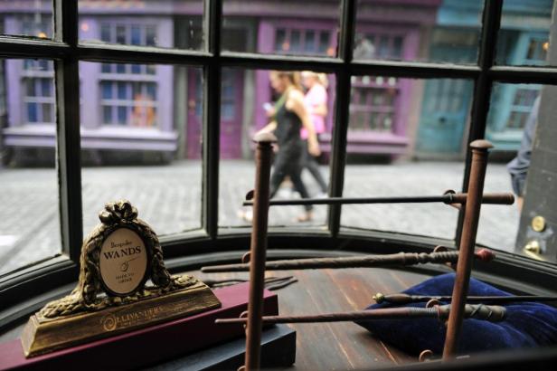 Ein Schaufenster von Ollivanders Zauberstabladen mit Zauberstäben und Passanten im Hintergrund.