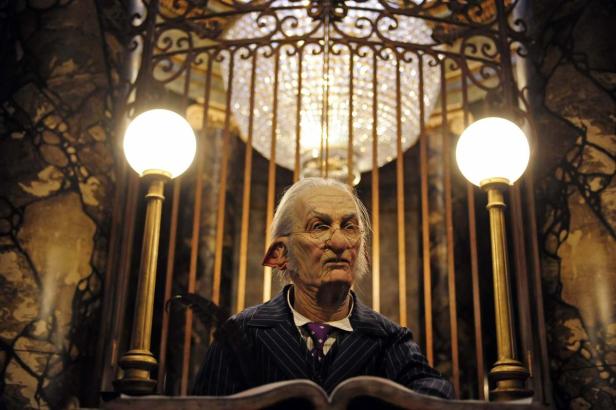 Ein Kobold sitzt in der Gringotts Bank, bewacht von zwei Laternen.