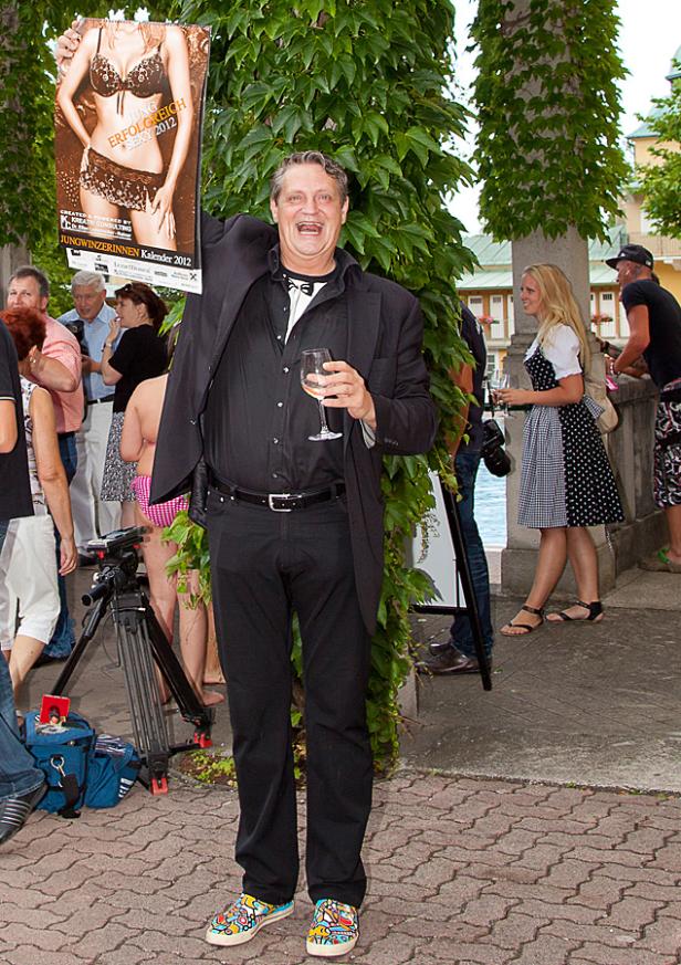 Ein Mann im Anzug präsentiert den „Jungwinzerinnen Kalender 2012“ und hält ein Weinglas.