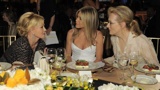 Melanie Griffith, Jennifer Aniston und Meryl Streep sitzen an einem Tisch bei einer Veranstaltung.