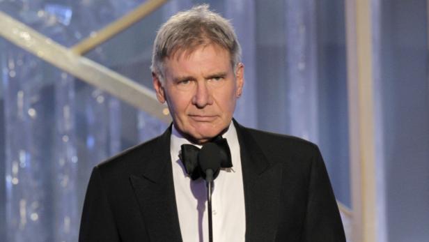 Harrison Ford in einem schwarzen Smoking vor einem Mikrofon.