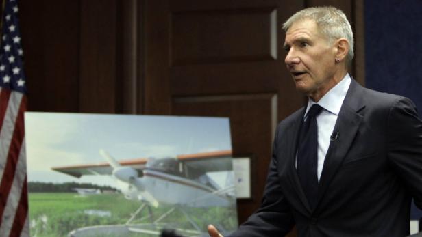 Harrison Ford spricht vor einem Foto eines Wasserflugzeugs.