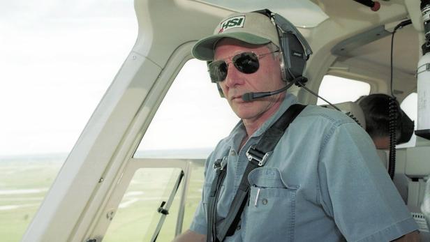 Harrison Ford sitzt im Cockpit eines Flugzeugs mit Headset und Sonnenbrille.