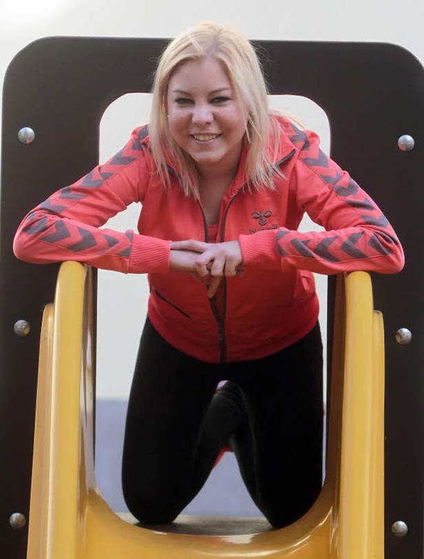 Eine blonde Frau kniet auf einer gelben Rutsche und lächelt.