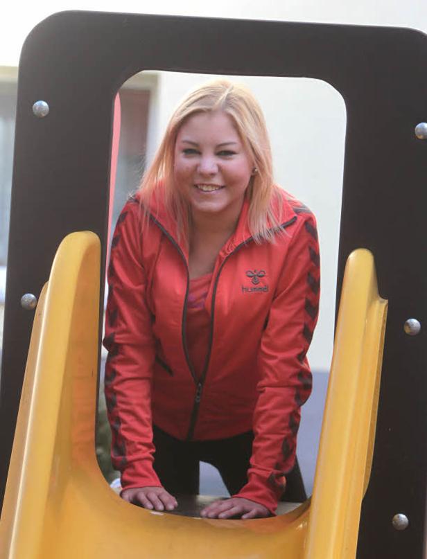 Eine Frau in roter Jacke lächelt, während sie auf einer gelben Rutsche steht.