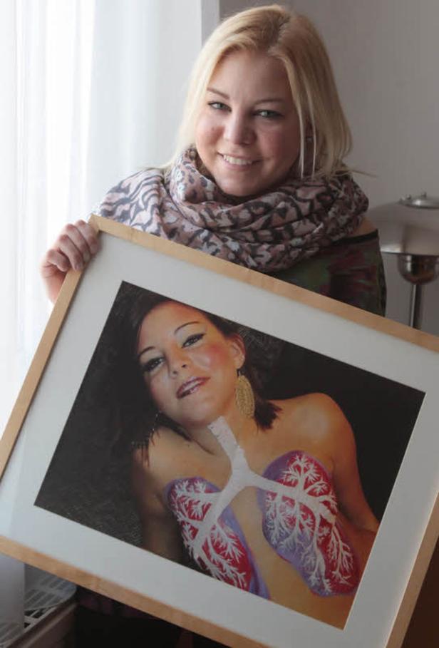 Eine Frau hält ein gerahmtes Bild von einer Frau mit aufgemalten Lungen auf der Brust.