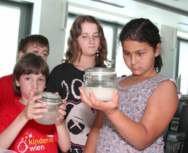 Vier Kinder betrachten ein Glas mit einer trüben Flüssigkeit.