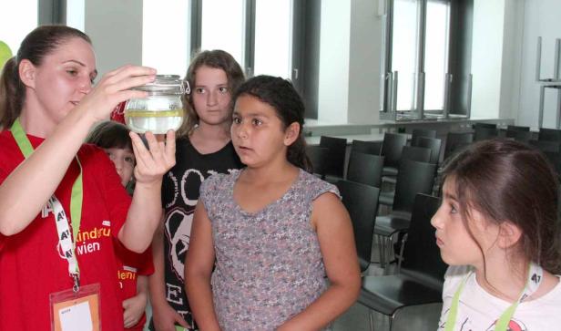 Eine Frau zeigt einer Gruppe von Kindern ein Glas mit einer Flüssigkeit darin.