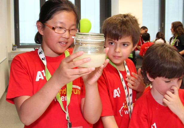 Kinder betrachten ein Glas mit einer trüben Flüssigkeit in einem Labor.