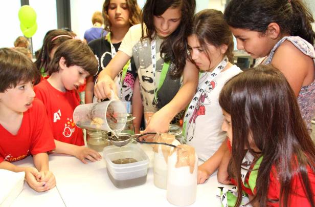 Eine Gruppe Kinder experimentiert mit Flüssigkeiten und Filtern an einem Tisch.