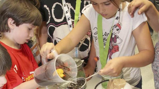 Kinder experimentieren mit einer Flüssigkeit und einem gelben Gummienten in einem Glas.