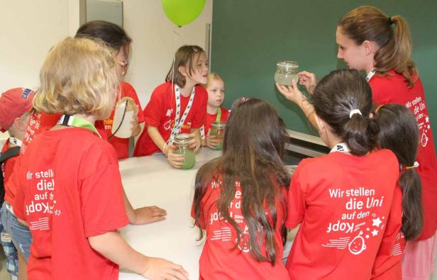 Eine Gruppe Kinder in roten T-Shirts experimentiert mit Gläsern und Flüssigkeiten.