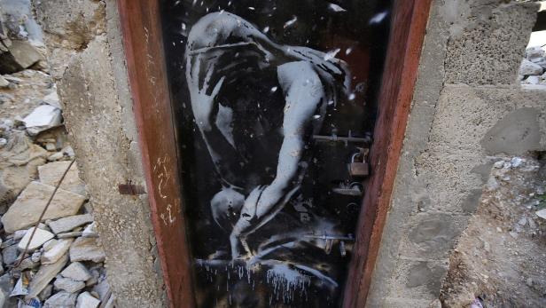 Ein Graffito an einer Tür in einem zerstörten Gebäude zeigt eine gebeugte, leidende Gestalt.