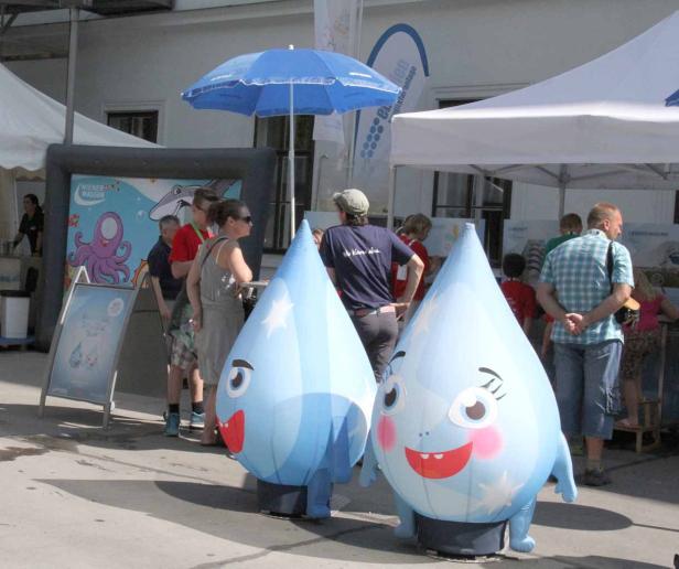 Zwei wassertropfenförmige Maskottchen stehen vor einem Stand von „Wiener Wasser“.