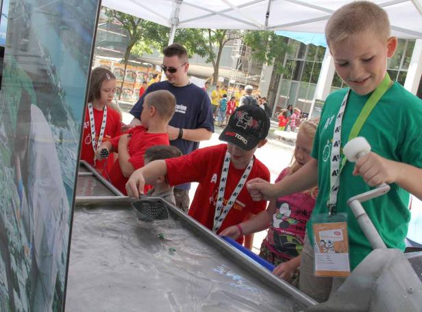 Kinder spielen an einem Wasserbecken mit kleinen Spielzeugen unter einem Zelt.