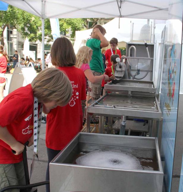 Kinder experimentieren mit Wasser an einem Stand im Freien.