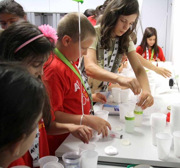 Eine Gruppe Kinder experimentiert mit Bechern und Flüssigkeiten auf einem Tisch.