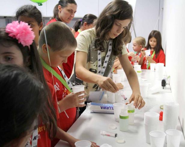 Eine Gruppe Kinder experimentiert mit Flüssigkeiten und Bechern an einem Tisch.