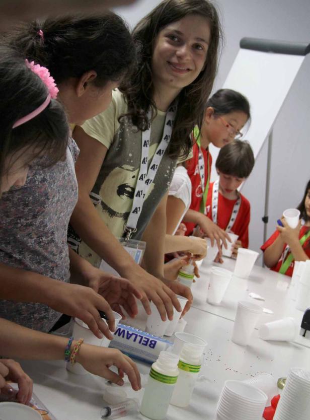 Eine Gruppe Kinder experimentiert mit Bechern und anderen Materialien an einem Tisch.