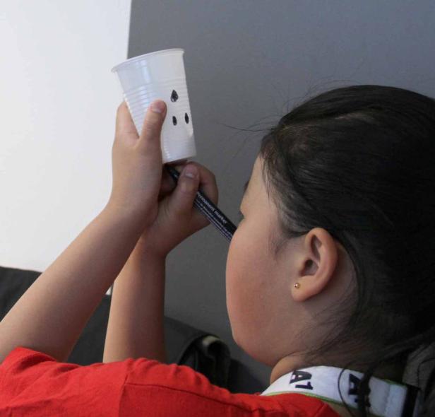 Ein Kind bemalt einen Plastikbecher mit einem schwarzen Stift.