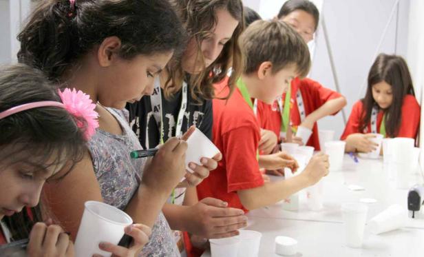 Eine Gruppe Kinder bemalt weiße Plastikbecher an einem Tisch.