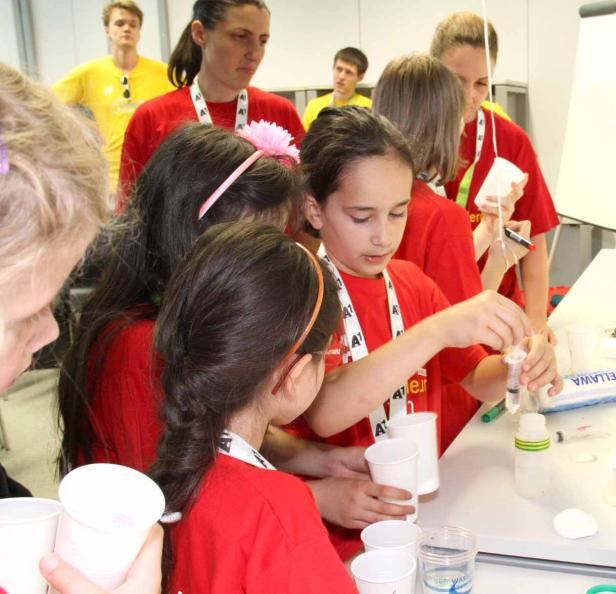 Eine Gruppe Kinder experimentiert mit Spritzen und Bechern an einem Tisch.