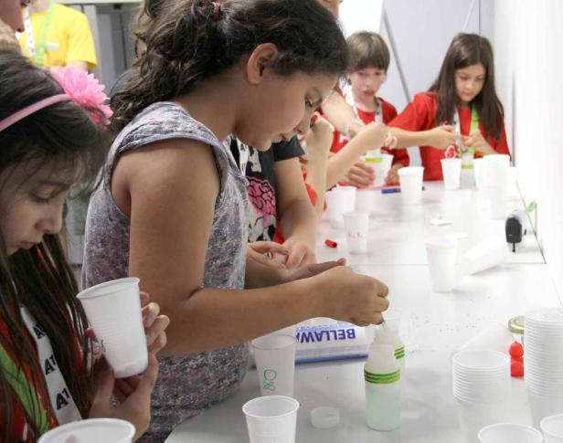 Eine Gruppe Kinder bastelt mit Bechern und kleinen Gegenständen an einem Tisch.