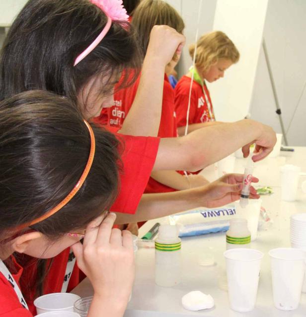 Kinder experimentieren mit Spritzen und Bechern an einem Tisch.