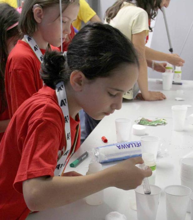 Ein Mädchen in einem roten T-Shirt experimentiert mit einer Spritze und Bechern.